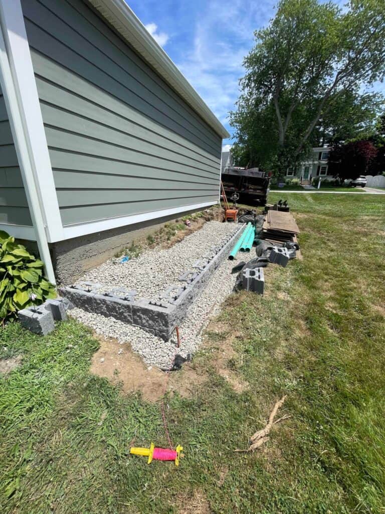 First course of retaining wall block set on crushed stone, with drainage pipe ready to go in behind it